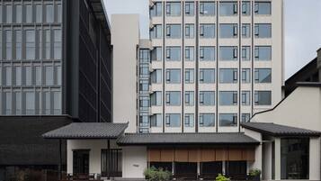 A modern hotel building with a prominent '6500' sign, featuring a mix of glass and concrete facade, and a traditional-style entrance with a stone pathway and greenery.