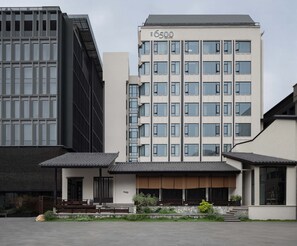 Ein modernes Hotelgebäude mit einem gut sichtbaren Schild mit der Aufschrift '6500', das eine Kombination aus Glas- und Betonfassade sowie einen klassisch gestalteten Eingangsbereich mit Steinweg und Bepflanzung aufweist.