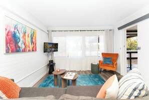 Un salon avec un canapé, un téléviseur, une petite table et un tableau coloré accroché au mur.