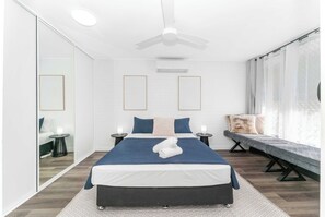 Une chambre moderne avec un lit, des tables de chevet, un banc et un ventilateur de plafond.