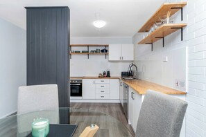 Une cuisine moderne avec des meubles blancs, un plan de travail en bois et une table à manger en verre.