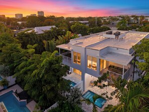 Une maison moderne à deux étages, dotée d’une terrasse sur le toit, d’une piscine et d’une végétation luxuriante.