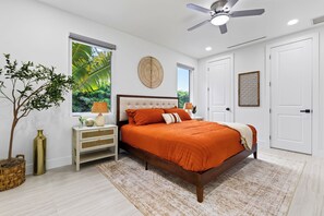 A bedroom with a large bed, a ceiling fan, a window with a view of greenery, a bedside table with a lamp, and a door. - Private Pool + Grill + Twin Homes | Victoria Park | Palm Perch + Palm Court (Fort Lauderdale)