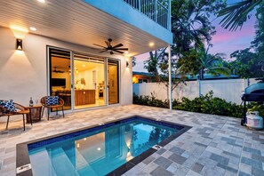 Une piscine avec une terrasse carrelée, un ventilateur de plafond et une vue sur une cuisine et un coin repas modernes.