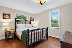 Un dormitorio con cama de madera, dos mesitas de noche, una lámpara de noche, ventana con vistas y una lámpara del techo.