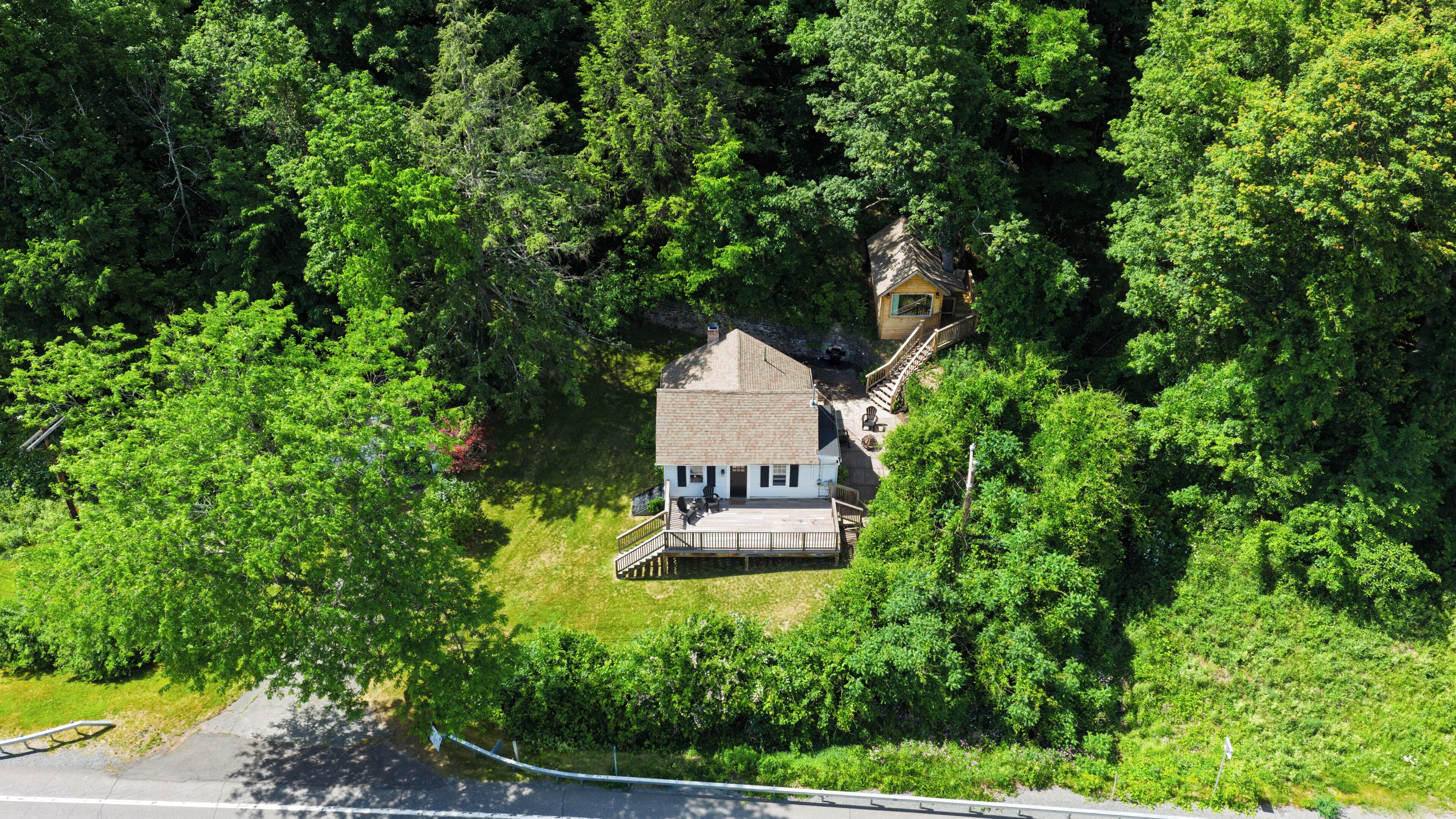 A house surrounded by dense forest, with a visible deck and a staircase leading to the entrance.