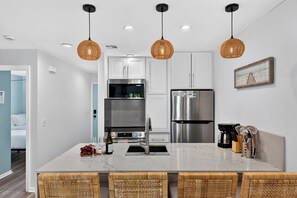 Cozinha moderna com bancada de mármore, eletrodomésticos de aço inoxidável, luminárias pendentes de vime e vista para um quarto.