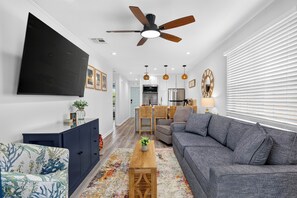 Una sala de estar moderna con ventilador de techo, televisor de pantalla plana, sofá, mesa de centro y comedor con muebles de mimbre.