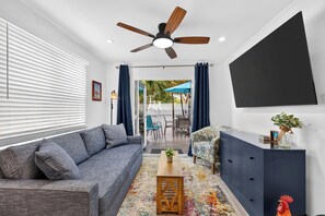 A living room with a grey sofa, a wooden coffee table, a blue cabinet, and a ceiling fan. - Shared Pool + Private Porch | Steps to Beach + Old Town | Salty Palm Retreat (Key West)