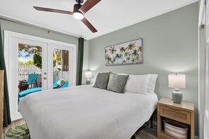 A bedroom with a large bed, two bedside tables with lamps, a ceiling fan, a door leading to a balcony, and a painting on the wall. - Shared Pool + Private Porch | Steps to Beach + Old Town | Salty Palm Retreat (Key West)