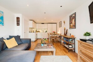 A modern living room with a grey sofa, wooden coffee table, and a dining area with a wooden table and chairs. - The Akerman Road Hideaway (London)