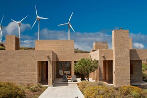 A modern building with multiple wind turbines, a paved walkway, and a seating area with a tree. - Casas Bioclimáticas Iter El Pueblo (Granadilla de Abona)