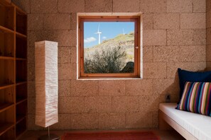 A room with a window, a bed, a wooden shelf, and a radiator. - Casas Bioclimáticas Iter El Pueblo (Granadilla de Abona)