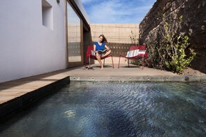 Eine Person sitzt auf einem roten Stuhl in der Nähe eines Pools mit einer Steinmauer und einem Holzdeck.