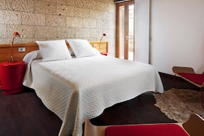 A bedroom with a bed, two bedside tables, a red chair, and a textured wall. - Casas Bioclimáticas Iter La Compacta (Granadilla de Abona)