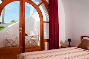 Ein Schlafzimmer mit einem Bett, einem Nachttisch, einer Lampe, einem Fenster mit Vorhängen und Blick auf einen Außenbereich mit Sitzgelegenheiten.