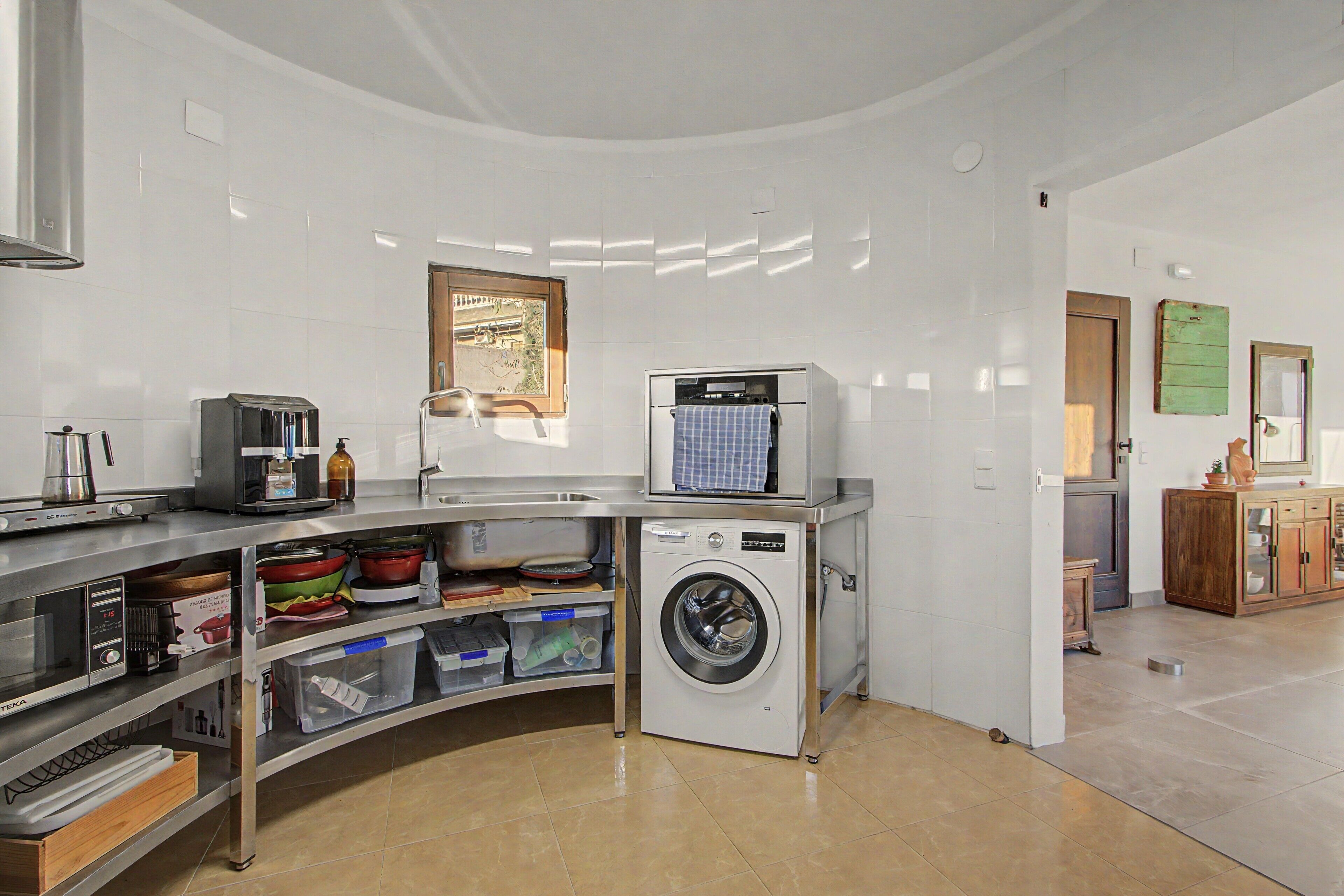 A compact kitchen with a built-in washing machine, a coffee machine, and a window with a view.