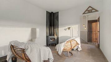 Een kamer met twee rieten stoelen bekleed met witte doeken, een open haard en een deur met een driehoekig houten frame.