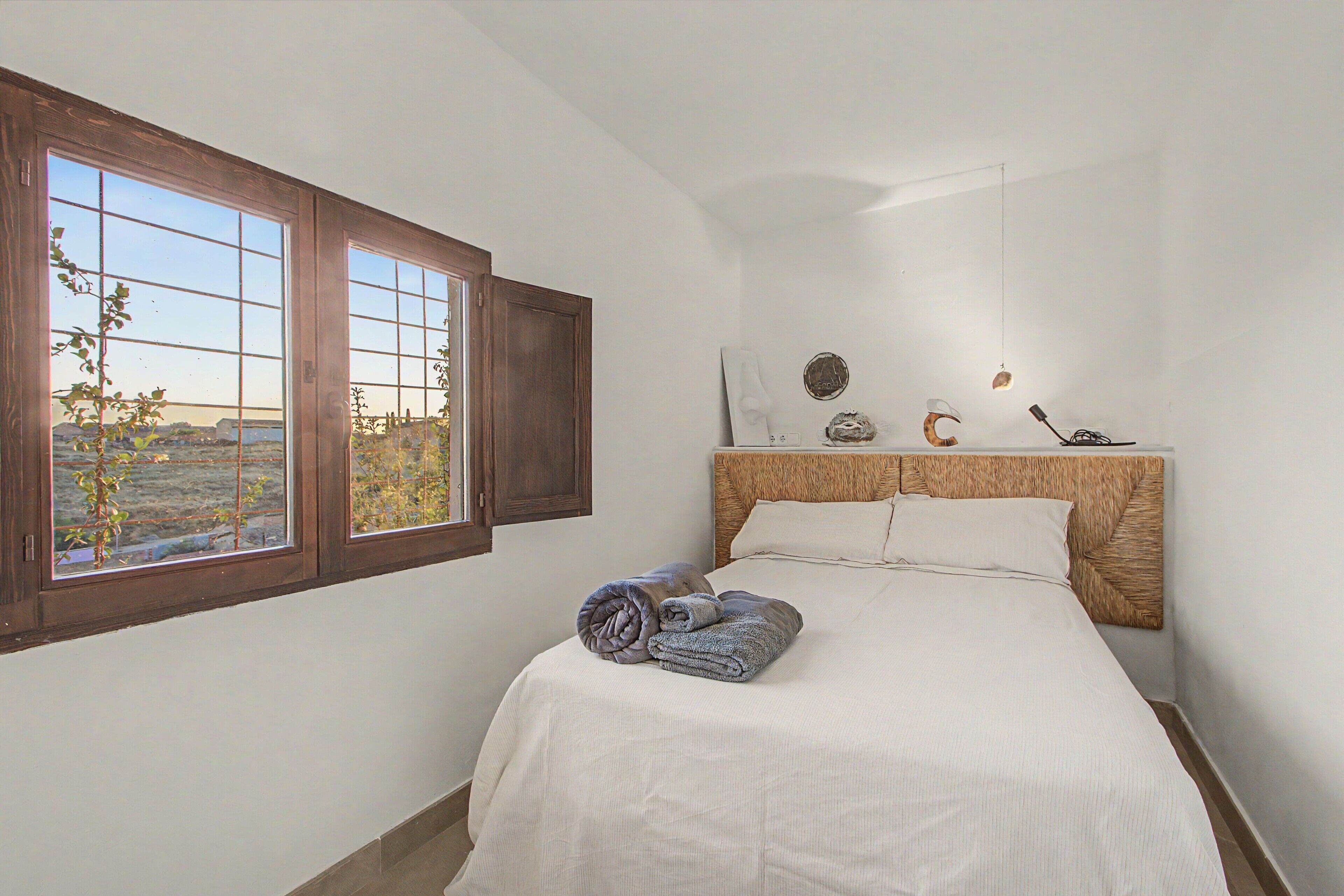 A bedroom with a large window, a bed with a headboard, and a view of the outdoors.