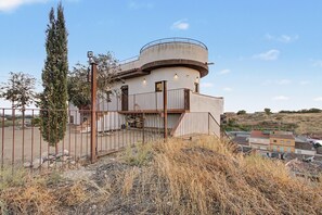 Un edificio circular con balcón, rodeado por una cerca y pastizales secos.