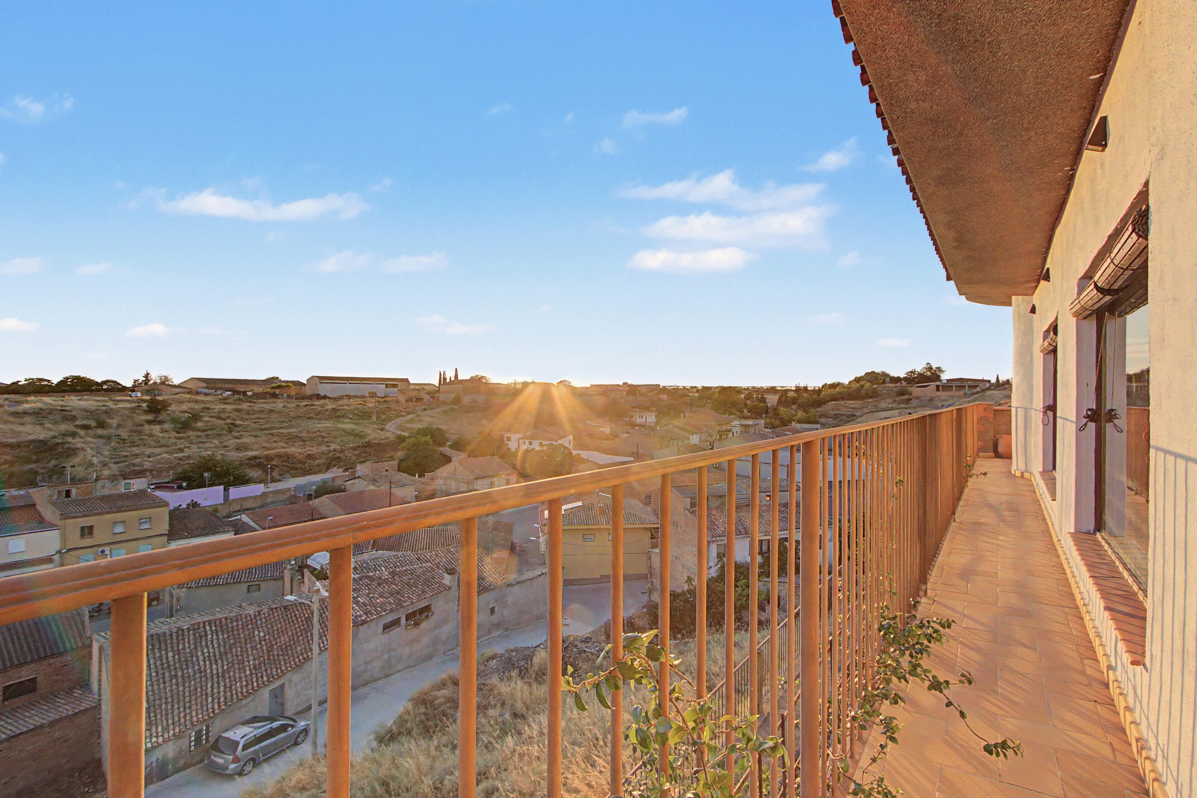 Un balcón con vistas a un pueblo, baranda de madera y un edificio con tejado de tejas.