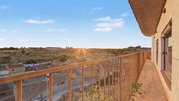 Un balcón con vistas a un pueblo, baranda de madera y un edificio con tejado de tejas.
