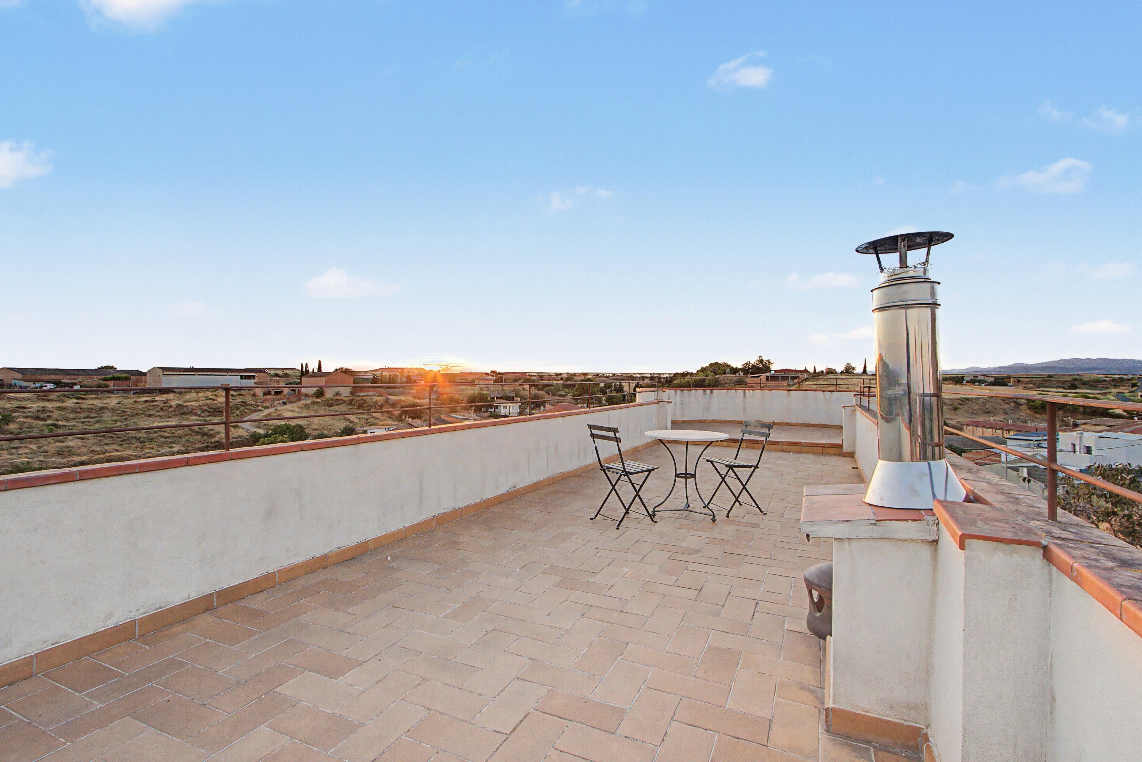 Un patio al aire libre con una mesa, sillas, un poste de luz metálico y vistas del paisaje.