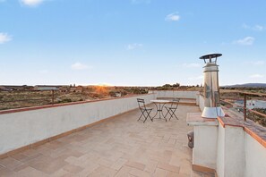 Un patio al aire libre con una mesa, sillas, un poste de luz metálico y vistas del paisaje.
