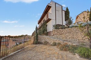 Un edificio moderno con un muro de contención de piedra, una valla metálica y un cielo despejado.