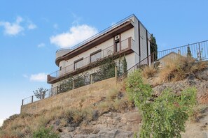 Un edificio de varios pisos con balcones, ubicado en una ladera con vegetación escasa.