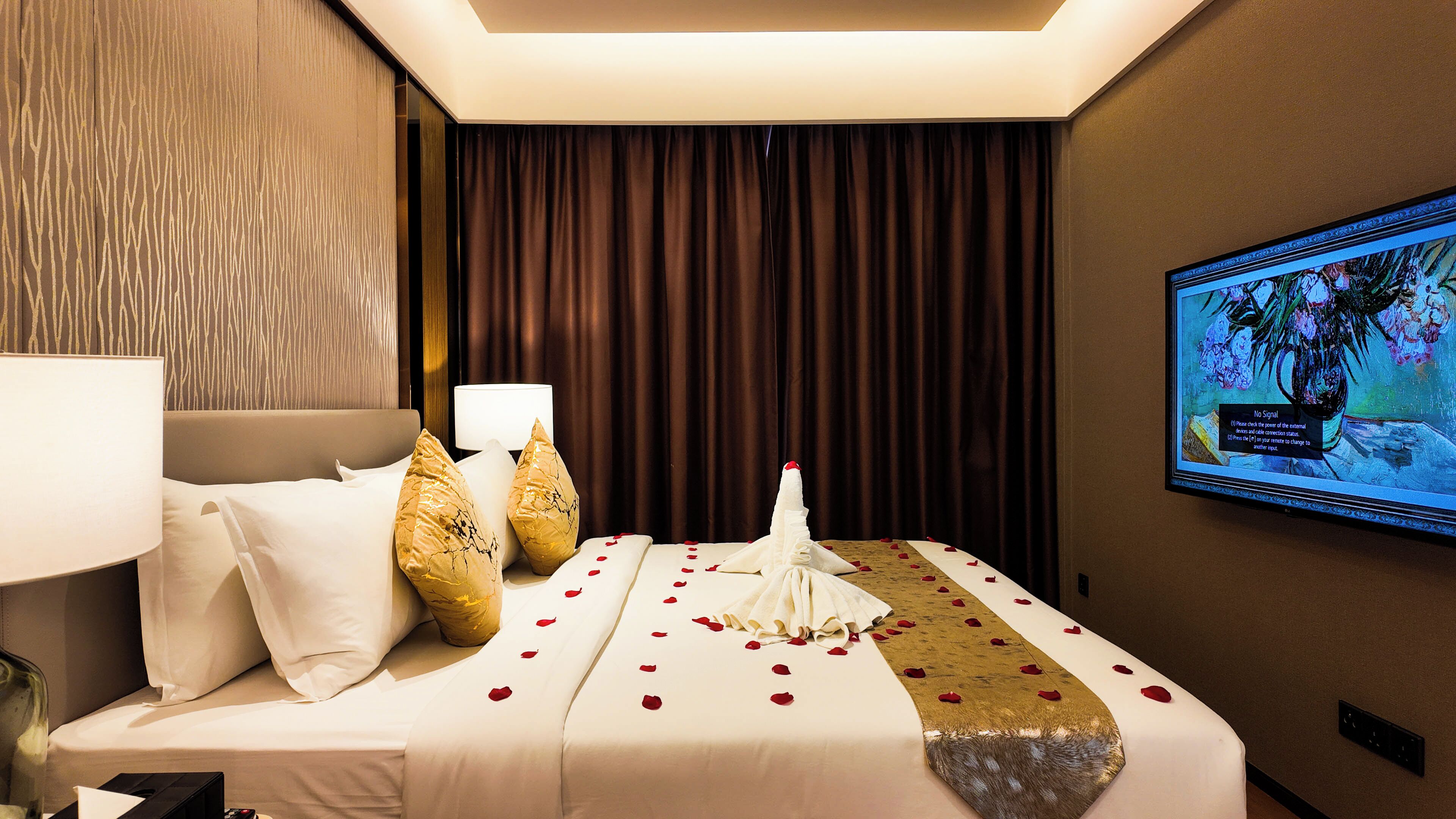 Ein Hotelzimmer mit Bett, Kissen, Nachttisch mit Lampe, Wandfernseher und Vorhang.