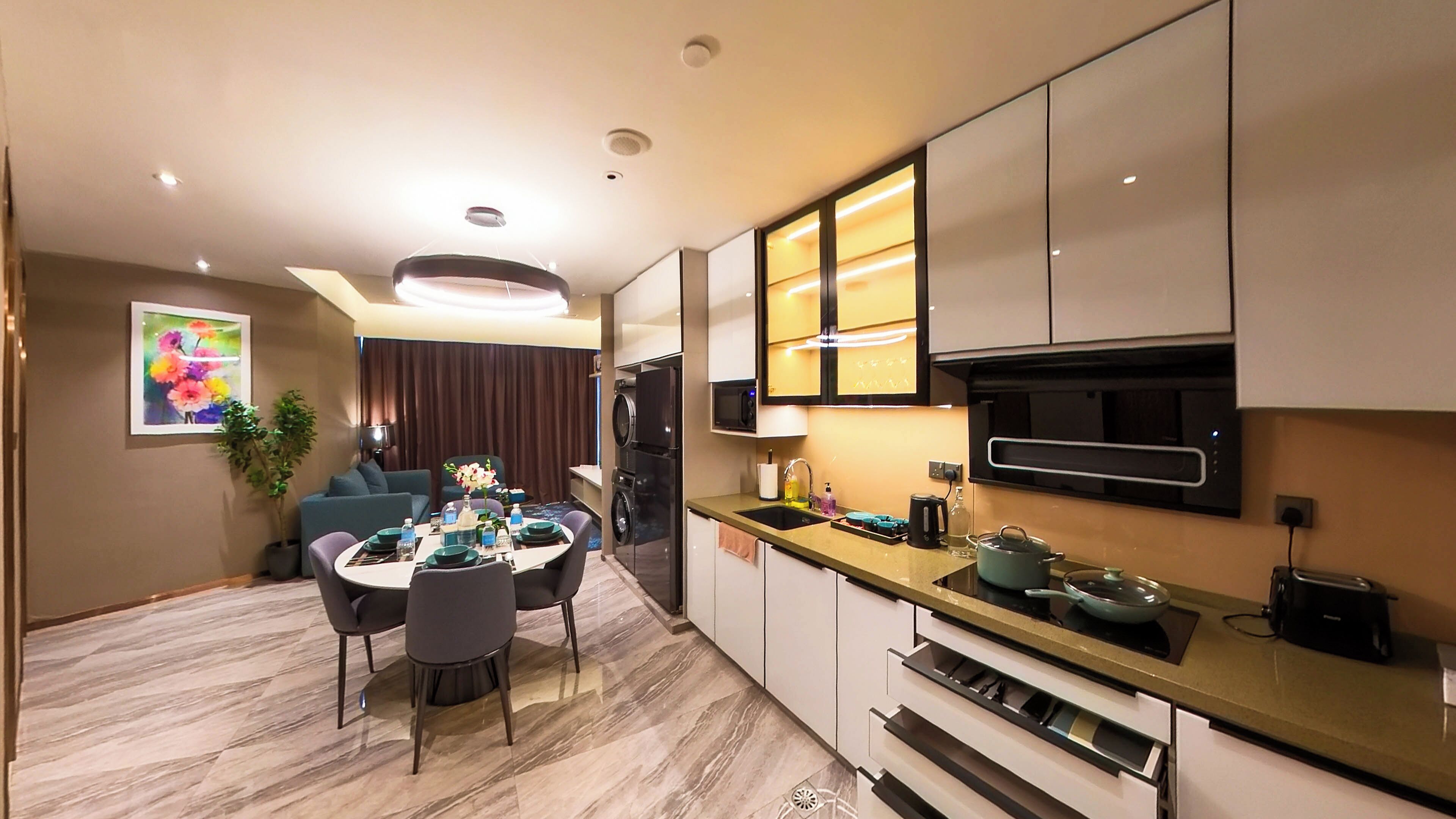 A modern kitchen with built-in appliances, a dining area with a table set for four, and a living area with a sofa and a potted plant.