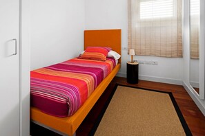 A single bed with an orange headboard, a colorful striped bedspread, and a small bedside table with a lamp. - Casas Bioclimáticas Iter El Muro (Granadilla de Abona)