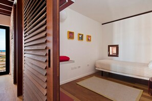 A bedroom with a bed, a red pillow, a wall-mounted shelf, and three framed pictures. - Casas Bioclimáticas Iter El Cubo (Granadilla de Abona)
