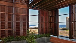A room with large windows, wooden shutters, and a view of the sea. - Casas Bioclimáticas Iter El Cubo (Granadilla de Abona)