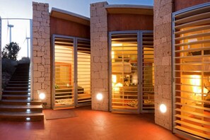 A modern building with stone walls and large glass doors leading to interior spaces. - Casas Bioclimáticas Iter La Estrella (Granadilla de Abona)