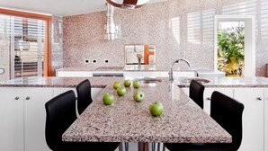 A modern kitchen with granite countertops, a stainless steel range hood, and a dining area with black chairs. - Casas Bioclimáticas Iter La Estrella (Granadilla de Abona)