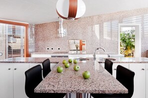 A modern kitchen with granite countertops, a stainless steel range hood, and a dining area with black chairs. - Casas Bioclimáticas Iter La Estrella (Granadilla de Abona)