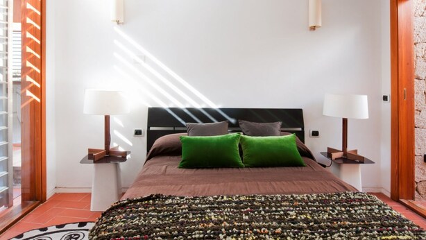 A bedroom with a bed, two bedside lamps, a patterned rug, and a view of the outside. - Casas Bioclimáticas Iter La Estrella (Granadilla de Abona)
