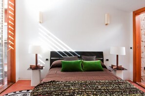 Ein Schlafzimmer mit einem Bett, zwei Nachttischlampen, einem gemusterten Teppich und Blick ins Freie.