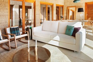 A modern living room with a white sofa, wooden rocking chairs, and a round table with a candle. - Casas Bioclimáticas Iter La Tea (Granadilla de Abona)
