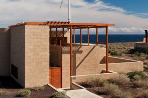 Un edificio moderno con una pérgola de madera, una puerta y vistas al océano.