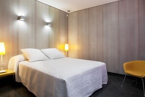 Ein Hotelzimmer mit einem Bett, Nachttischlampen, einem Sessel und einer Wandleuchte.