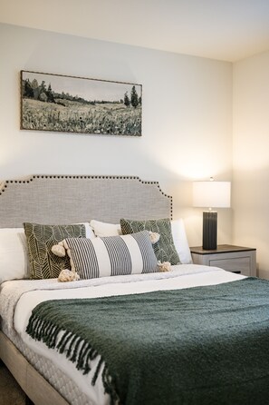 Una cama bien hecha con una manta verde, varios almohadones y un cabecero con adornos decorativos.