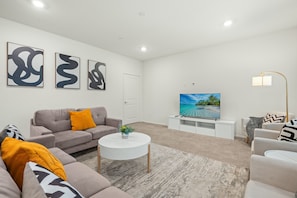 Una sala de estar moderna con un sofá gris, una mesa de centro blanca y un televisor de pantalla plana sobre un mueble blanco.