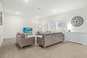A modern living room with a grey sofa set, a flat-screen TV, a white dresser, and a wall clock.