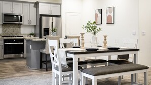 Una cucina moderna con elettrodomestici in acciaio inossidabile, una zona pranzo con tavolo e sedie bianche e una piccola pianta in vaso.