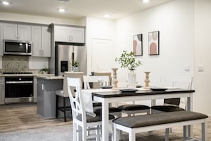 Una cocina moderna con electrodomésticos de acero inoxidable, un comedor con mesa y sillas blancas, y una pequeña planta en maceta.