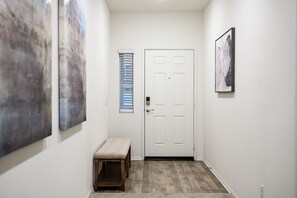Un couloir avec une porte blanche, un banc et deux tableaux accrochés aux murs.