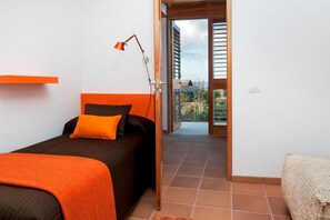 A bedroom with a bed, an orange accent wall, a bedside lamp, and a view through an open door to an outdoor balcony. - Casas Bioclimáticas Iter Casa Bernouilli (Granadilla de Abona)